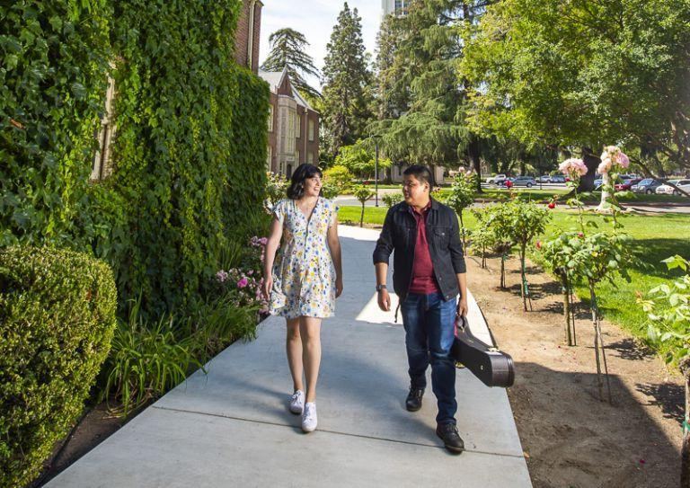 male student with cello case and female student walking under brick arch covered with ivy